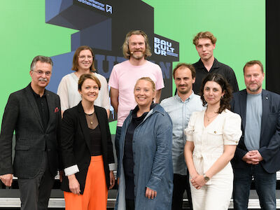 7. UrbanSlam! der AKNW (v. l.): Ernst Uhing (Präsident AKNW), Patrycja Muc (Moderatorin, vorne), Anna Michelle Ußler (Gewinnerin), Kilian Kresing, Prof. Judith Reitz (PBSA), Max Salzberger, Christopher Neuwirth, Profi-Slammerin Meral Ziegler und Peter Köddermann (Geschäftsführer Programm Baukultur NRW). Foto: Mathias Kehren