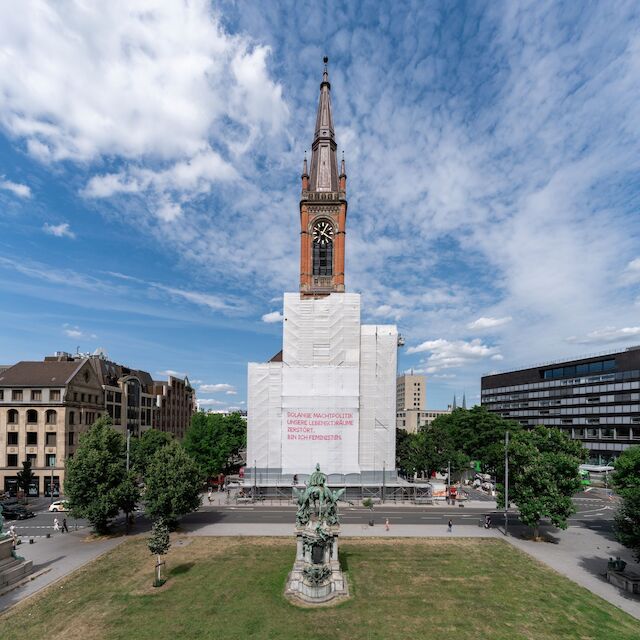 Auf Einladung der Architektinnen Initiative NW realisierte die österreichische Künstlerin Katharina Cibulka ihr 33. SOLANGE Netz an der Evangelischen Johanneskirche in Düsseldorf. Durch das überdimensionale, mit pinkem Tüll im Kreuzstich applizierte Statement wird auf gender-basierte Missstände aufmerksam gemacht.